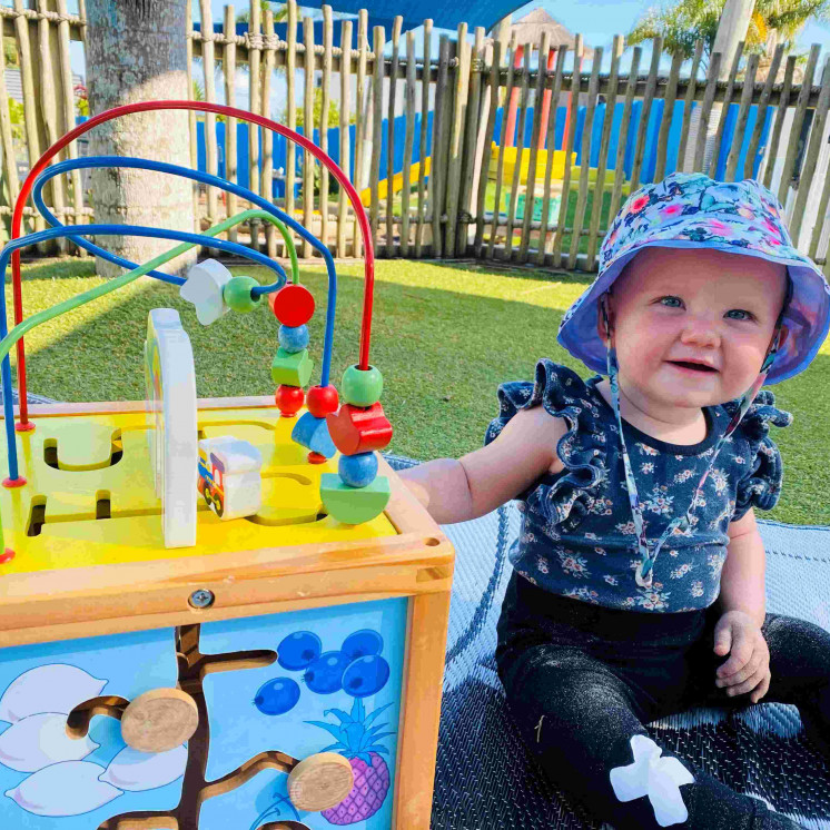 Baby playing outside with puzzle at Busy Bees Coopers Beah