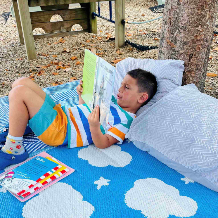 Kindergarten child enjoying quite time reading in the shade at Busy Bees Mount Wellington